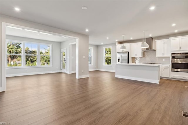 kitchen with a kitchen island, appliances with stainless steel finishes, pendant lighting, white cabinets, and wall chimney range hood