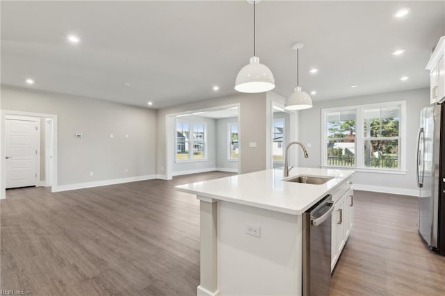 kitchen featuring white cabinetry, sink, hanging light fixtures, stainless steel appliances, and a center island with sink