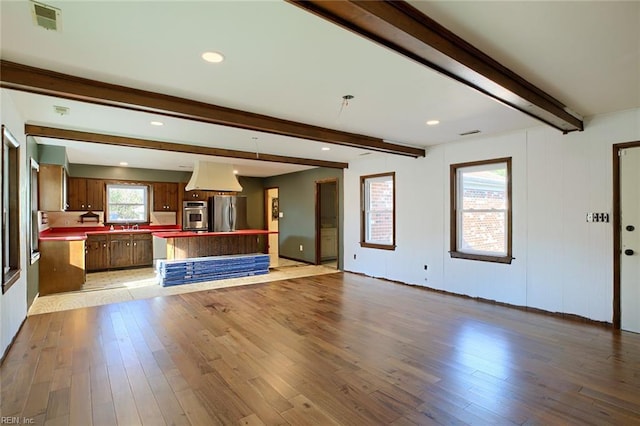 unfurnished living room with sink, beam ceiling, and light hardwood / wood-style floors