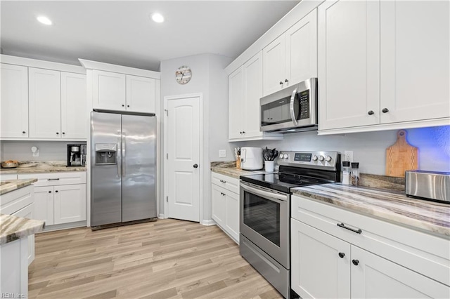 kitchen featuring light stone countertops, stainless steel appliances, white cabinets, and light wood-type flooring