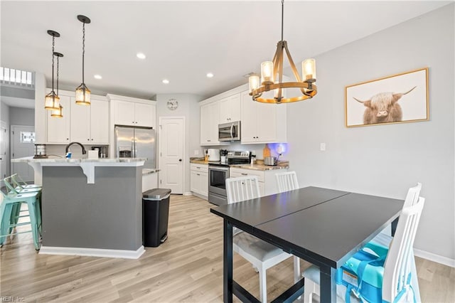 kitchen featuring light hardwood / wood-style flooring, stainless steel appliances, white cabinets, a kitchen bar, and decorative light fixtures