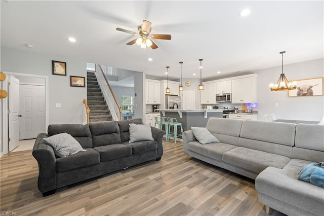 living room with ceiling fan with notable chandelier and light hardwood / wood-style floors