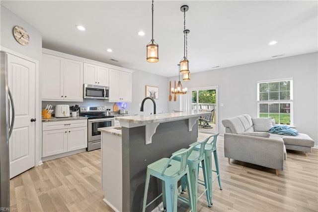 kitchen with pendant lighting, a breakfast bar area, appliances with stainless steel finishes, white cabinetry, and light stone countertops