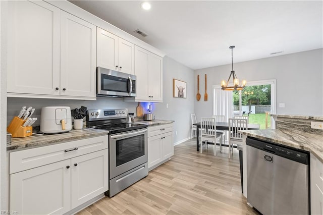 kitchen with pendant lighting, white cabinetry, stainless steel appliances, light stone countertops, and light wood-type flooring