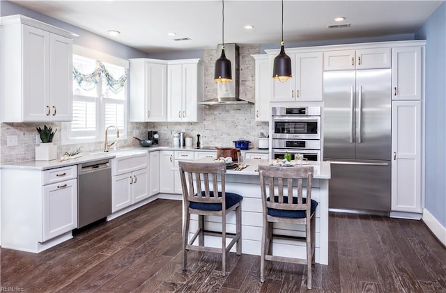 kitchen with appliances with stainless steel finishes, pendant lighting, white cabinets, a center island, and wall chimney range hood