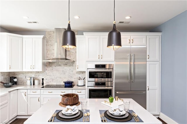 kitchen featuring stainless steel appliances, pendant lighting, wall chimney range hood, and white cabinets