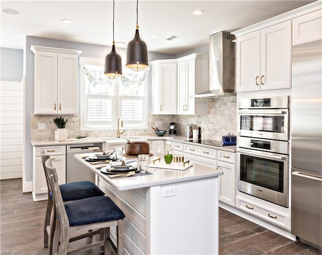 kitchen with pendant lighting, wall chimney range hood, white cabinetry, stainless steel appliances, and a center island