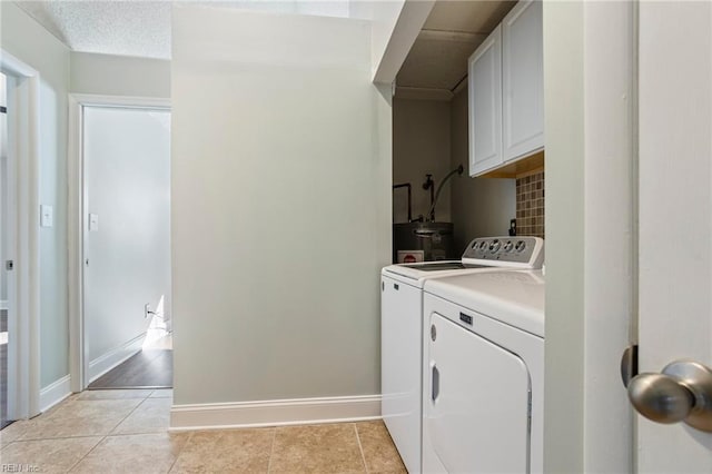 clothes washing area with cabinets, washing machine and clothes dryer, water heater, and light tile patterned floors