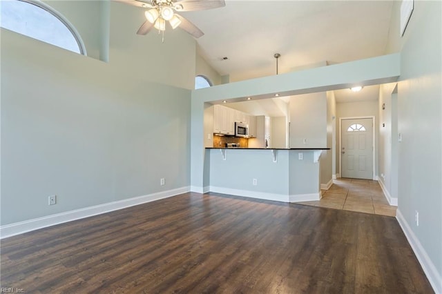 unfurnished living room with wood-type flooring, ceiling fan, and high vaulted ceiling