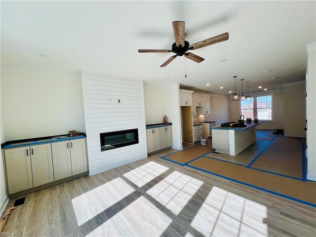 unfurnished living room with ceiling fan, sink, a large fireplace, and light wood-type flooring