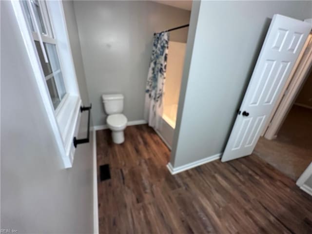 bathroom with hardwood / wood-style flooring, shower / bathtub combination with curtain, and toilet