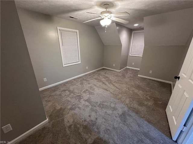 additional living space featuring dark colored carpet, ceiling fan, vaulted ceiling, and a textured ceiling