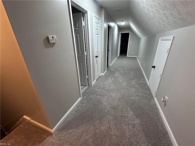 corridor featuring lofted ceiling, a textured ceiling, and dark colored carpet