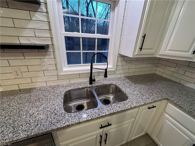 interior details featuring light stone countertops, sink, white cabinets, and backsplash