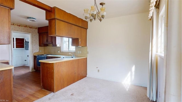 kitchen with pendant lighting, tasteful backsplash, sink, stove, and an inviting chandelier