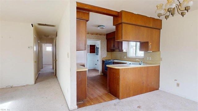 kitchen featuring sink, tasteful backsplash, an inviting chandelier, stainless steel range, and kitchen peninsula