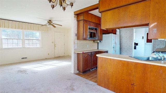 kitchen featuring sink, backsplash, carpet floors, white refrigerator with ice dispenser, and ceiling fan with notable chandelier