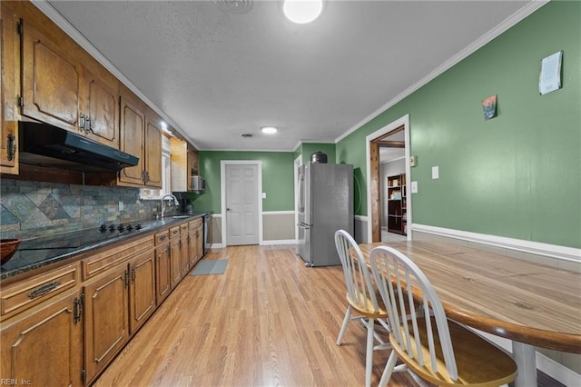 kitchen featuring sink, light hardwood / wood-style flooring, stainless steel refrigerator, dark stone countertops, and black electric cooktop