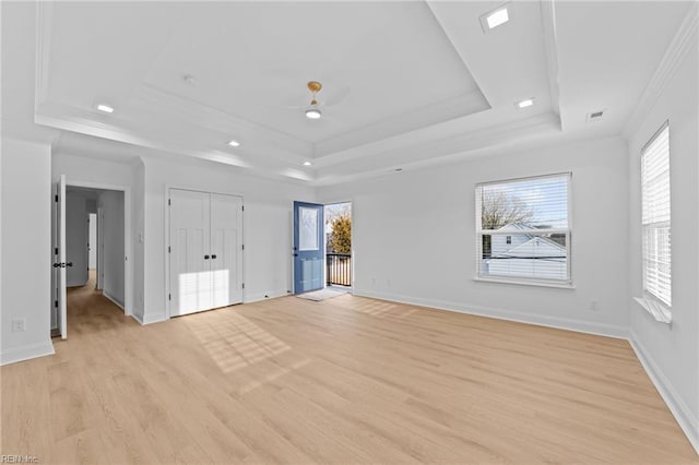 interior space with crown molding, a raised ceiling, multiple windows, and light wood-type flooring