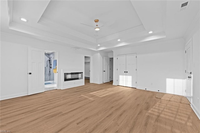 unfurnished living room with ceiling fan, ornamental molding, a tray ceiling, and light hardwood / wood-style flooring