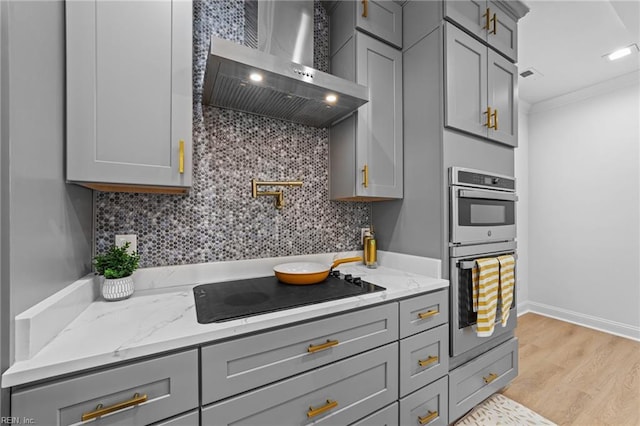 kitchen with crown molding, gray cabinets, wall chimney exhaust hood, black electric cooktop, and stainless steel double oven