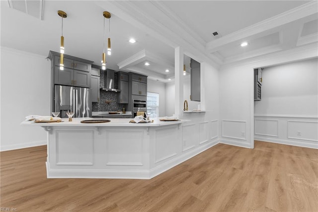 kitchen with hanging light fixtures, ornamental molding, appliances with stainless steel finishes, kitchen peninsula, and wall chimney range hood