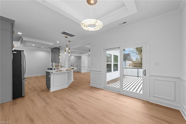 kitchen with hanging light fixtures, ornamental molding, stainless steel fridge, gray cabinets, and an island with sink