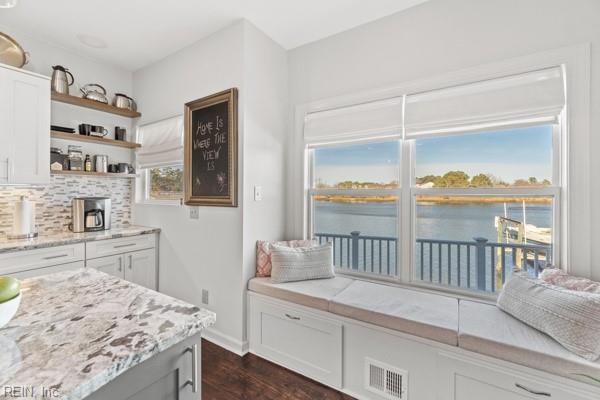 kitchen featuring dark hardwood / wood-style floors, a water view, light stone counters, white cabinets, and decorative backsplash