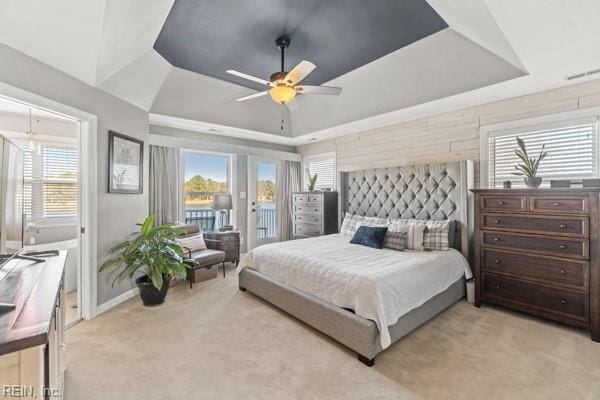 bedroom featuring access to exterior, a tray ceiling, light colored carpet, and ceiling fan