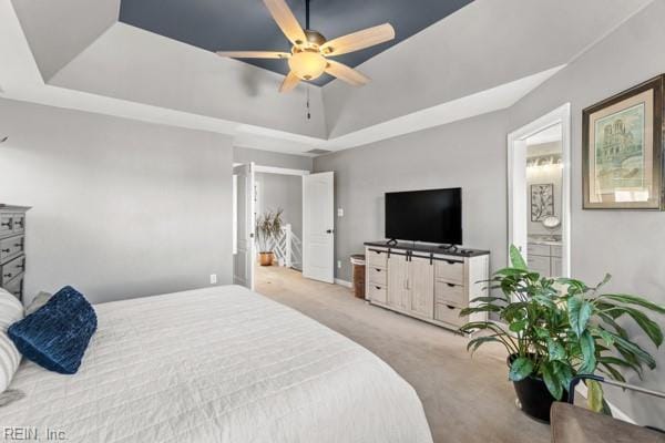 bedroom featuring light carpet, ensuite bath, a raised ceiling, and ceiling fan