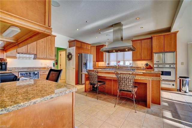 kitchen featuring light tile patterned flooring, appliances with stainless steel finishes, island range hood, wine cooler, and a kitchen breakfast bar