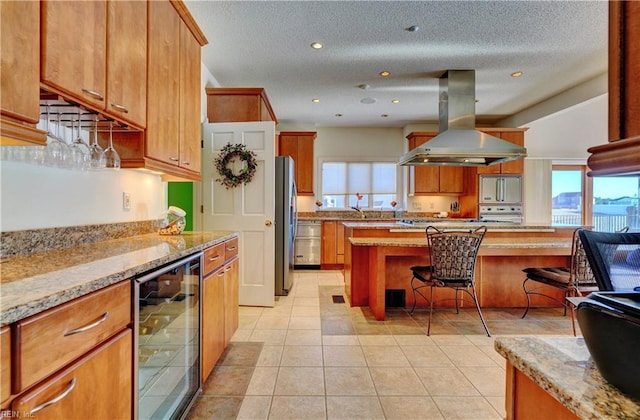 kitchen with light tile patterned floors, a breakfast bar area, wine cooler, island range hood, and light stone countertops