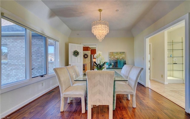 dining area with hardwood / wood-style floors, a notable chandelier, and vaulted ceiling