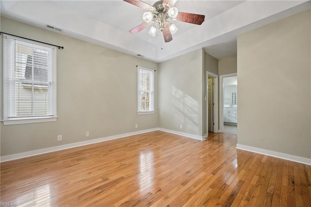 spare room with a tray ceiling, ceiling fan, and light wood-type flooring