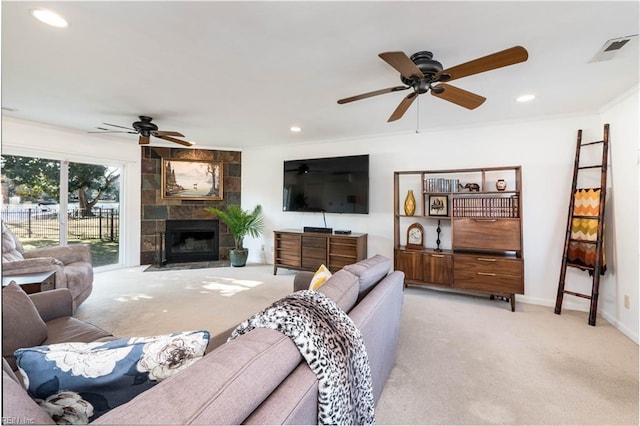 carpeted living room featuring a tiled fireplace, crown molding, and ceiling fan