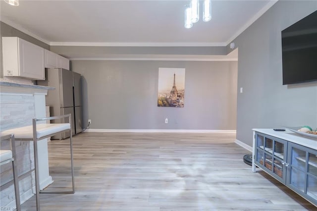 kitchen with stainless steel refrigerator, ornamental molding, light wood-type flooring, and white cabinets