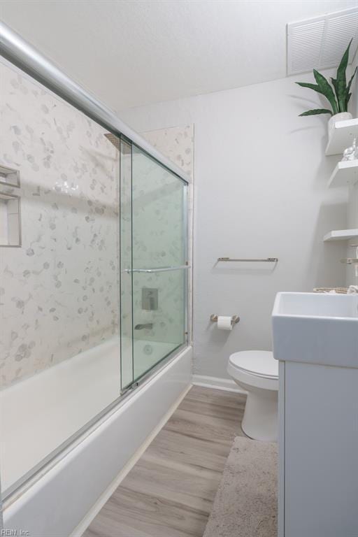 full bathroom with vanity, hardwood / wood-style floors, bath / shower combo with glass door, and toilet