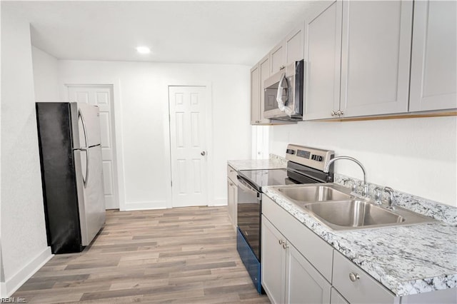 kitchen with appliances with stainless steel finishes, sink, and light hardwood / wood-style flooring