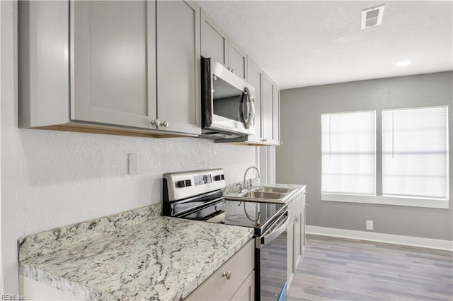 kitchen featuring sink, gray cabinetry, light stone counters, stainless steel appliances, and light hardwood / wood-style flooring