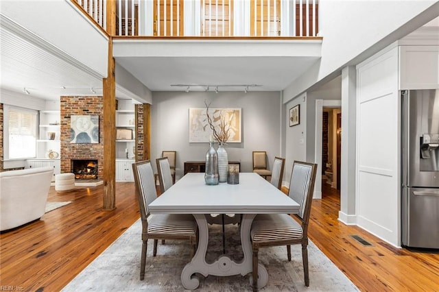 dining space with rail lighting, a high ceiling, a fireplace, light hardwood / wood-style floors, and built in shelves