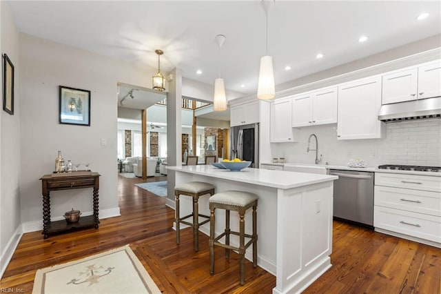 kitchen with sink, appliances with stainless steel finishes, white cabinetry, a kitchen island, and decorative light fixtures