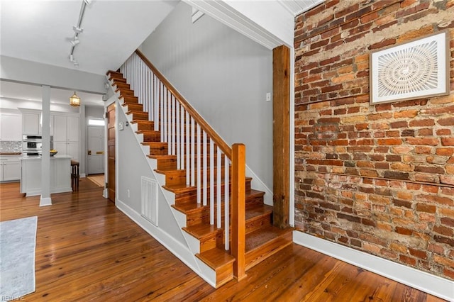 staircase featuring brick wall, hardwood / wood-style floors, and track lighting