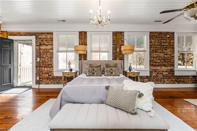 bedroom with access to exterior, ceiling fan with notable chandelier, wood-type flooring, and brick wall