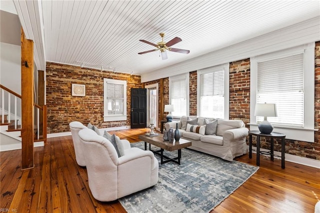 living room featuring ceiling fan, plenty of natural light, wood-type flooring, and brick wall