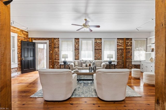 living room with hardwood / wood-style flooring, track lighting, ceiling fan, and brick wall