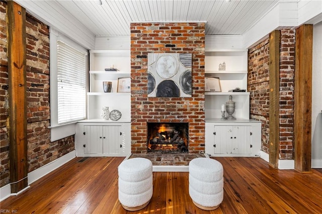 unfurnished living room with dark wood-type flooring, a fireplace, built in features, and brick wall