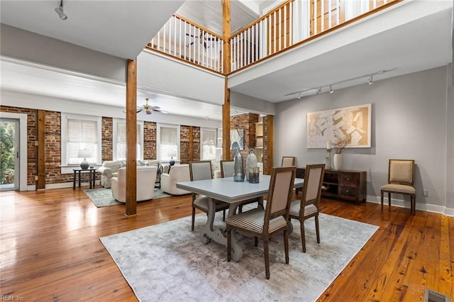 dining room featuring a high ceiling, hardwood / wood-style flooring, ceiling fan, and brick wall