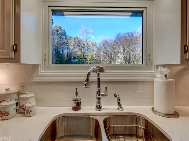 interior details featuring light stone counters, white cabinetry, sink, and decorative backsplash