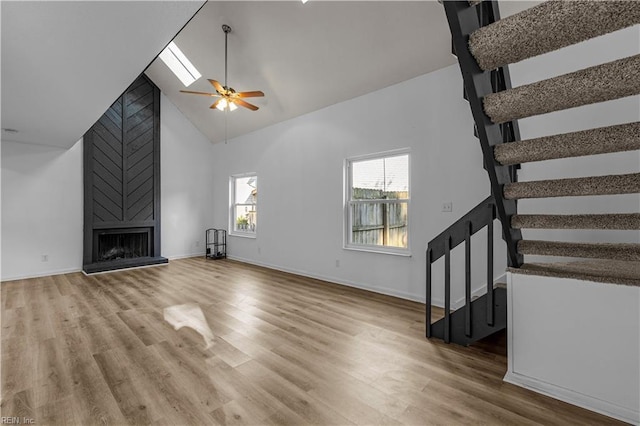 unfurnished living room featuring ceiling fan, a large fireplace, hardwood / wood-style floors, and high vaulted ceiling