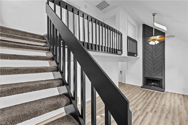 stairs featuring a high ceiling, ceiling fan, hardwood / wood-style flooring, and a fireplace